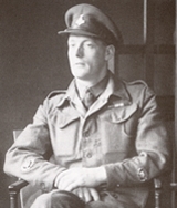Stan Hollis VC sits for a portrait painting wearing battledress and his gallantry and campaign medal ribbons in 1946.